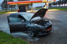 Automobilist blust eigen auto met poederblusser van tankstation