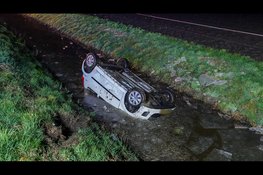 Auto ondersteboven in sloot op spiegelgladde weg, bestuurster met spoed naar ziekenhuis